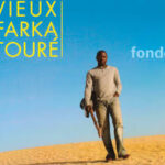 Cover: Vieux Farka Toure, Fondo. Shows the singer carrying a guitar on a sand dune.